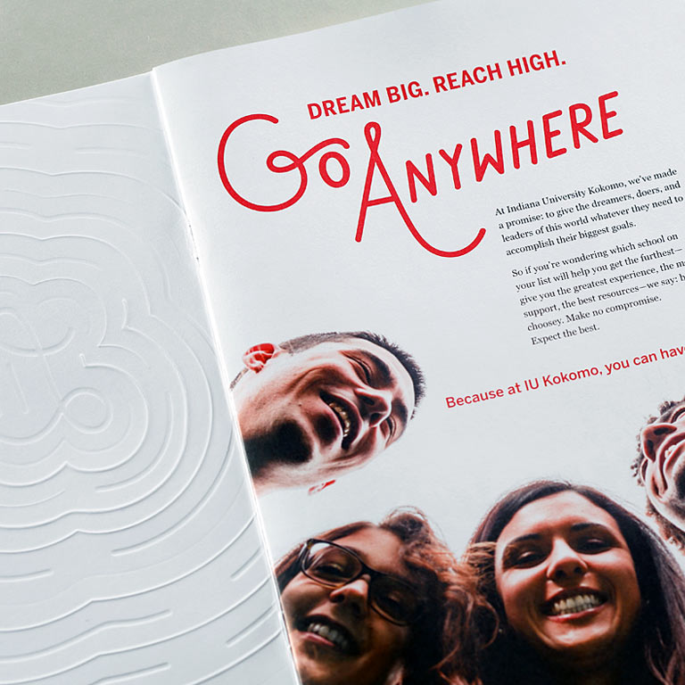 A spread from the IU Kokomo viewbook shows the inside of the embossed cover and students with the words 'Dream big. Reach high' and 'Go anywhere' on the first page.